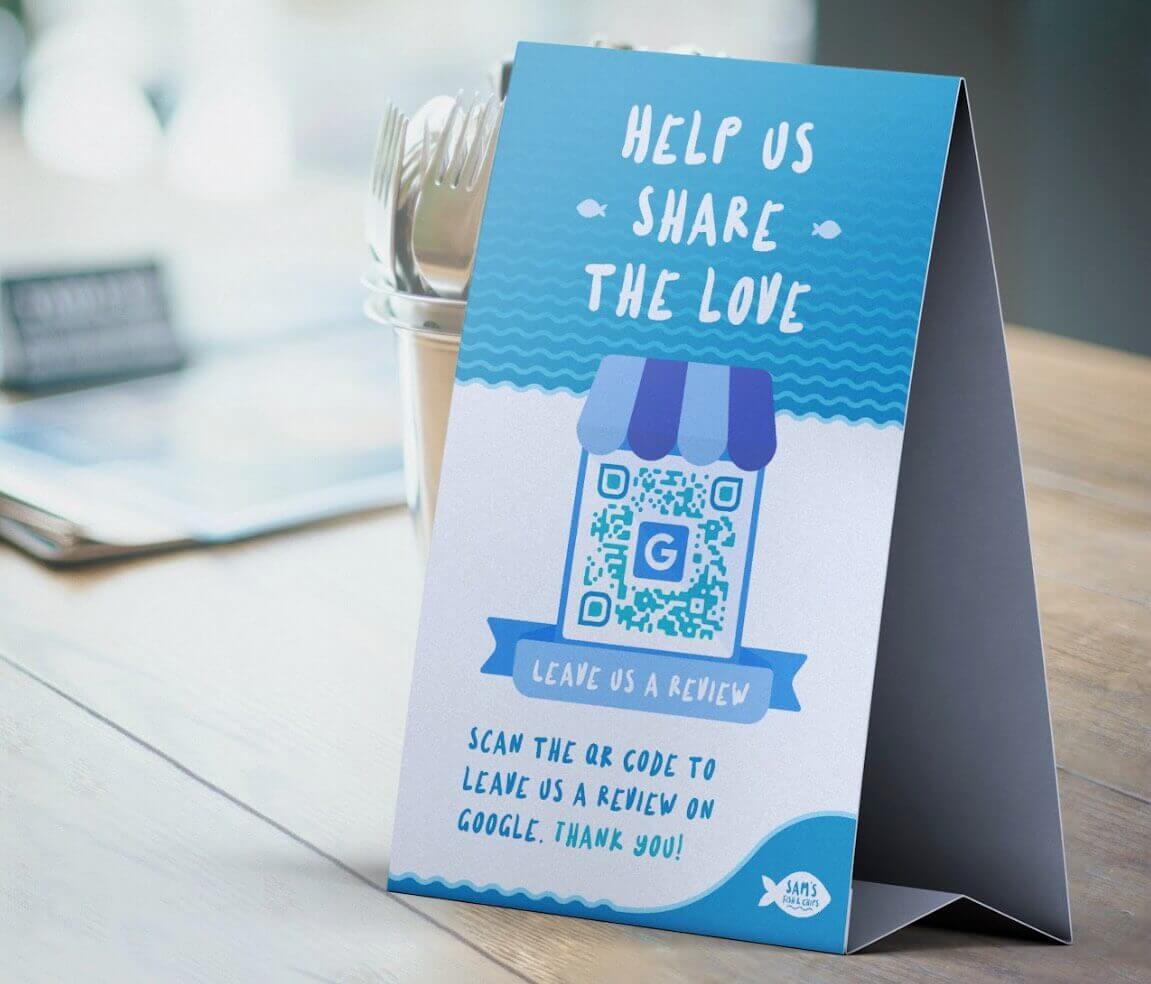 A blue and white table tent with a QR Code on top and a “Leave us a review” call to action.